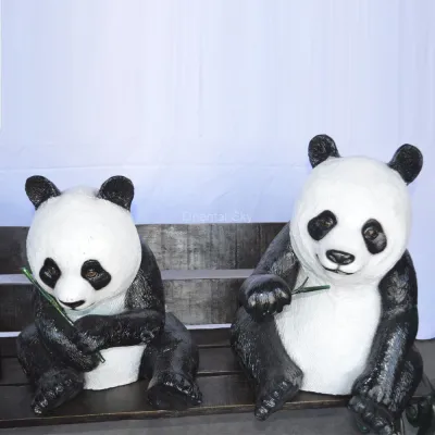 Три бронзовых статуи медведей панды, сидящие на садовой скульптуре скамейки