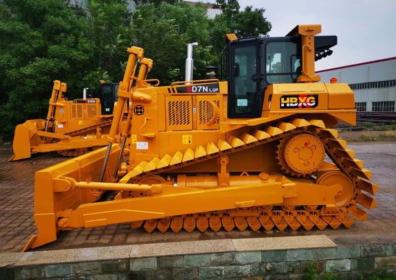 A motor grader, resembling the skilled artisan of road construction, levels and grades surfaces with meticulous detail, ensuring the safety and reliability of transportation routes.